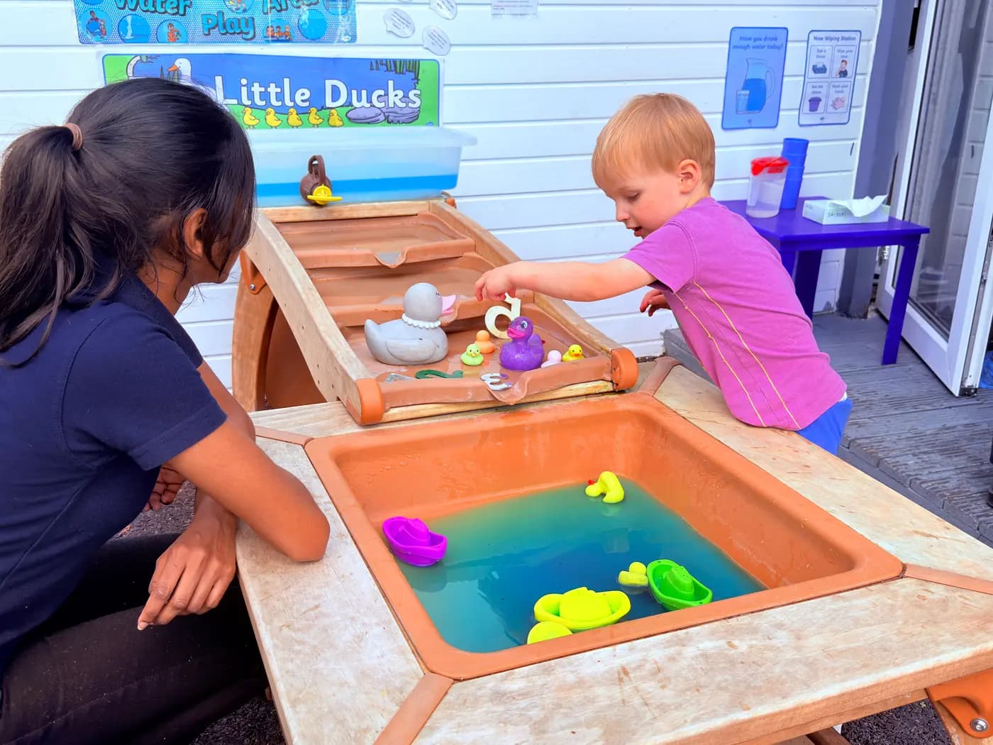 Toddler at the Little Ducks water-play table with a Blue Nest Montessori Harrow teacher