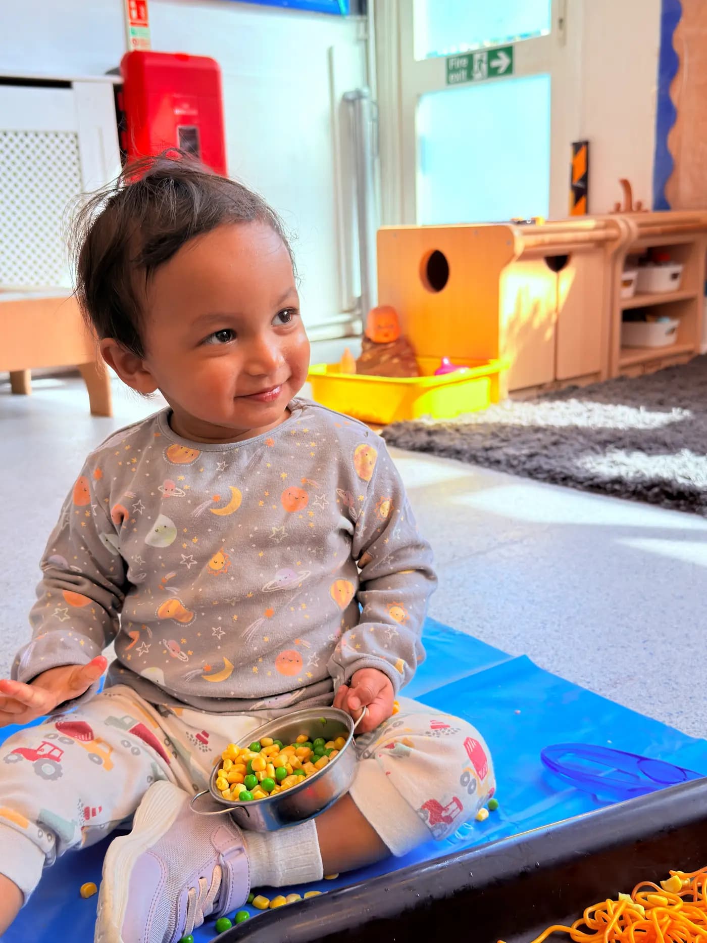 Smiling toddler with a food sensory tray at Blue Nest Montessori Harrow